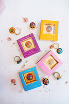Flatlay arrangement of Song of India complete solid perfume collection showing colorful boxes in pink, blue, yellow and purple with opened brass containers and floral accents