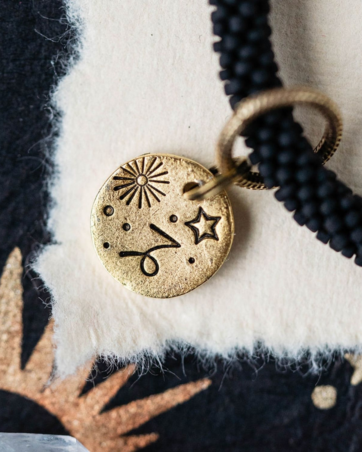 Close-up gold Capricorn zodiac charm with goat horn engravings attached to black beaded bracelet