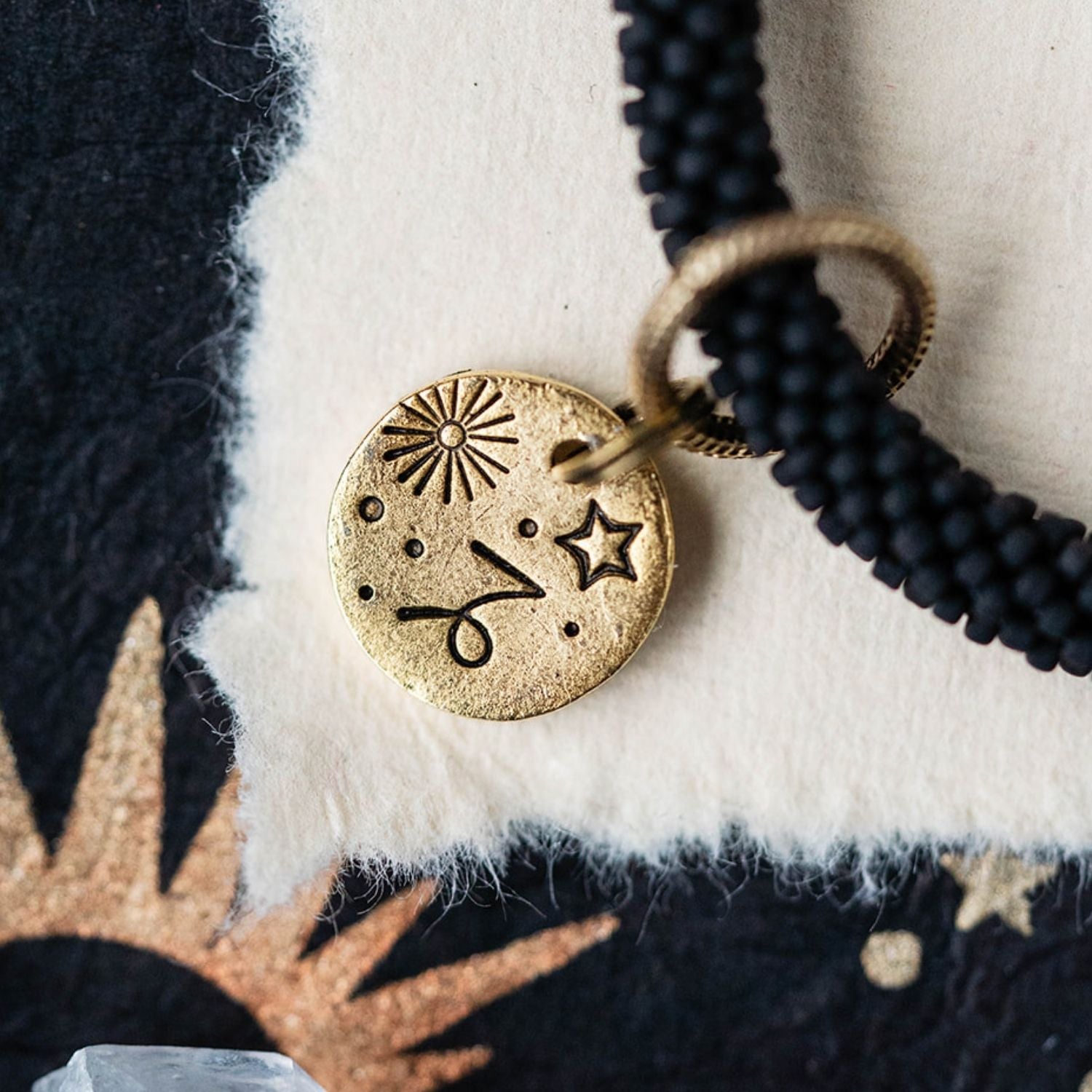 Close-up gold Capricorn zodiac charm with goat horn engravings attached to black beaded bracelet