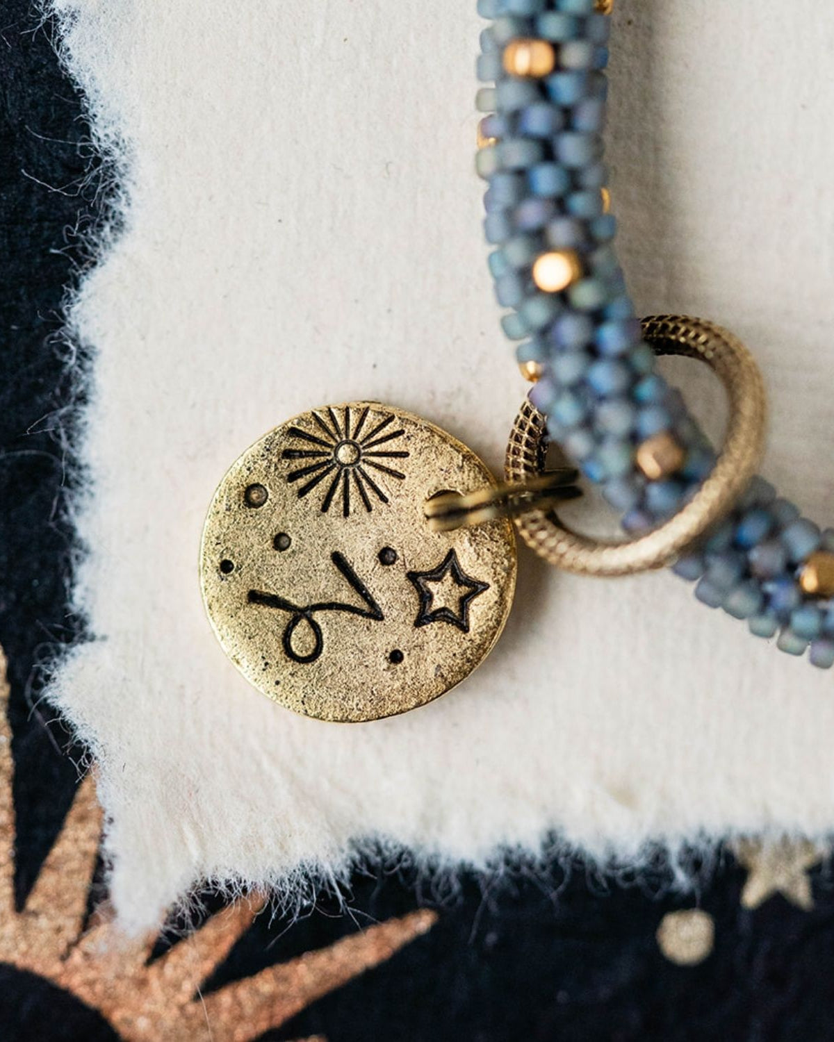 Gold Capricorn charm with blue-grey beaded jewelry showing goat constellation and sun engravings