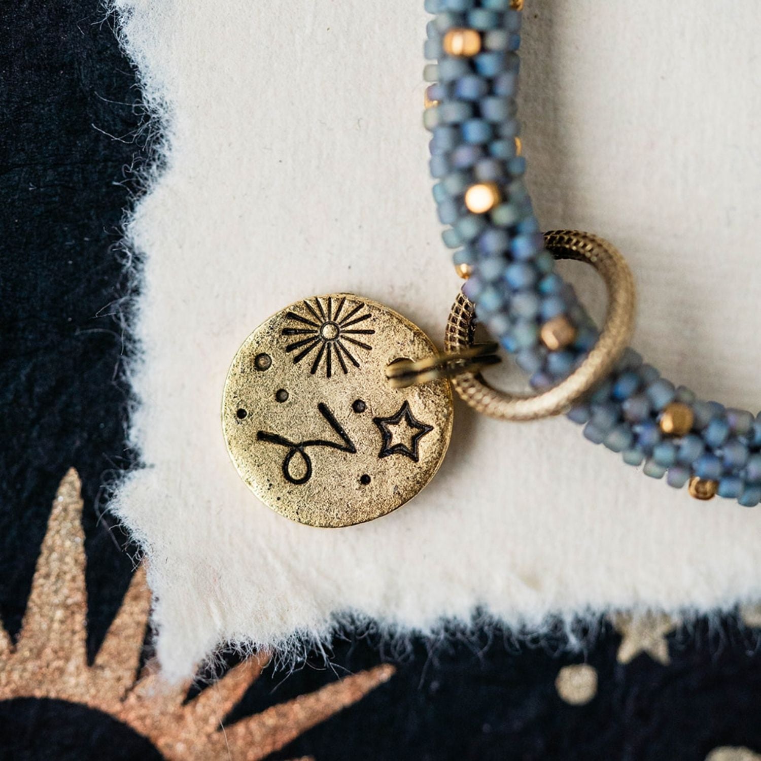 Gold Capricorn charm with blue-grey beaded jewelry showing goat constellation and sun engravings