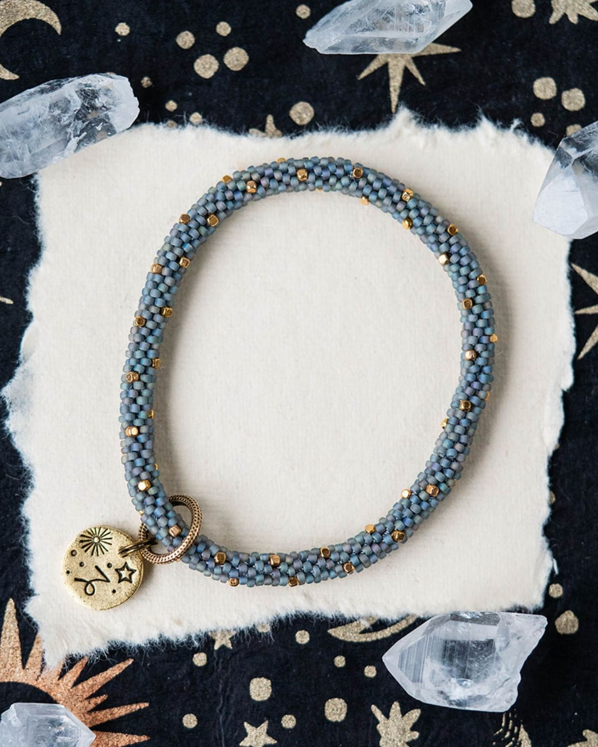 Blue-grey beaded bracelet with gold spacers and Capricorn zodiac charm on celestial background
