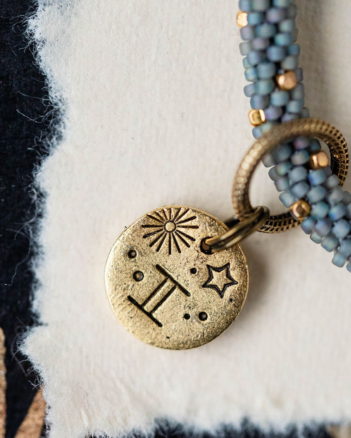 Gold Gemini charm with blue-grey beaded strands showing twins constellation and sun engravings