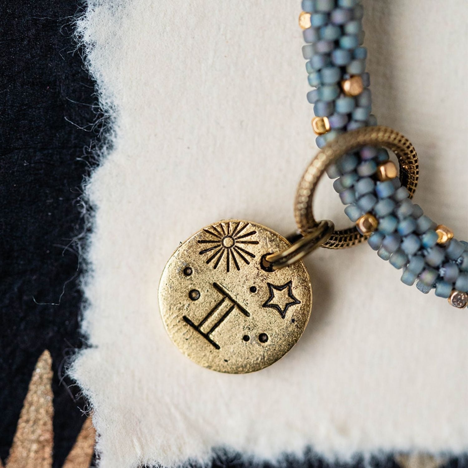 Gold Gemini charm with blue-grey beaded strands showing twins constellation and sun engravings