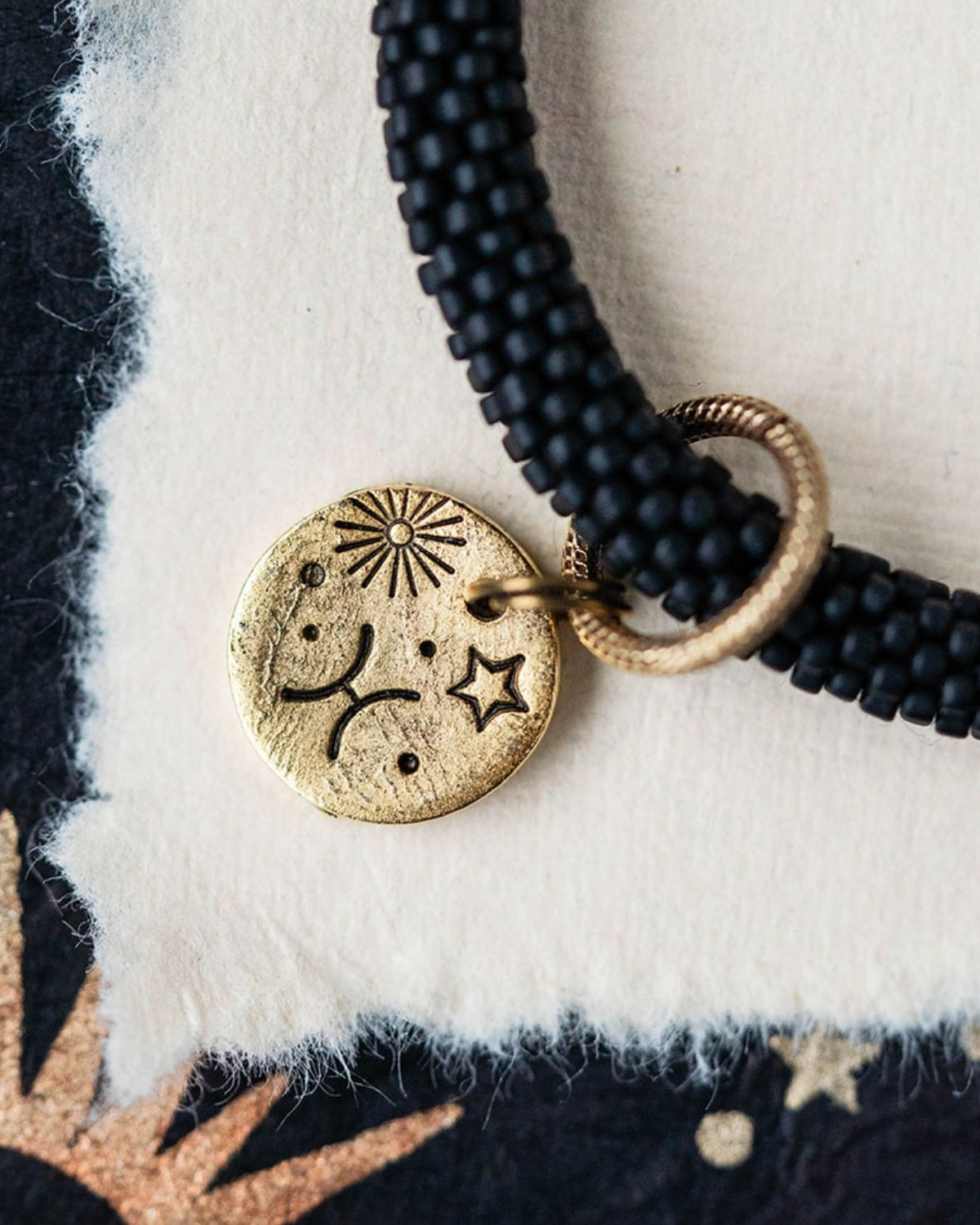 Close-up gold Pisces zodiac charm with fish symbols attached to black beaded bracelet detail