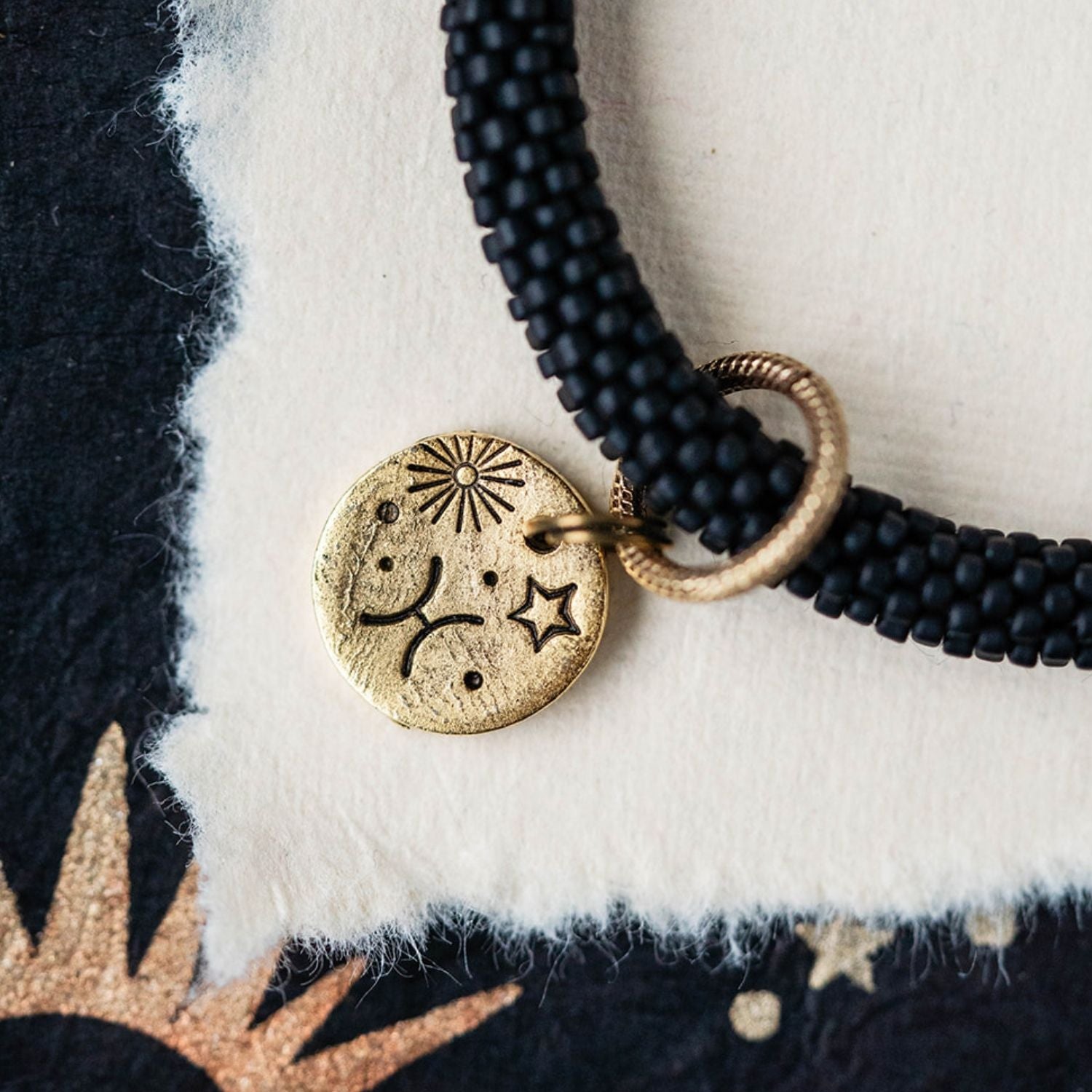 Close-up gold Pisces zodiac charm with fish symbols attached to black beaded bracelet detail