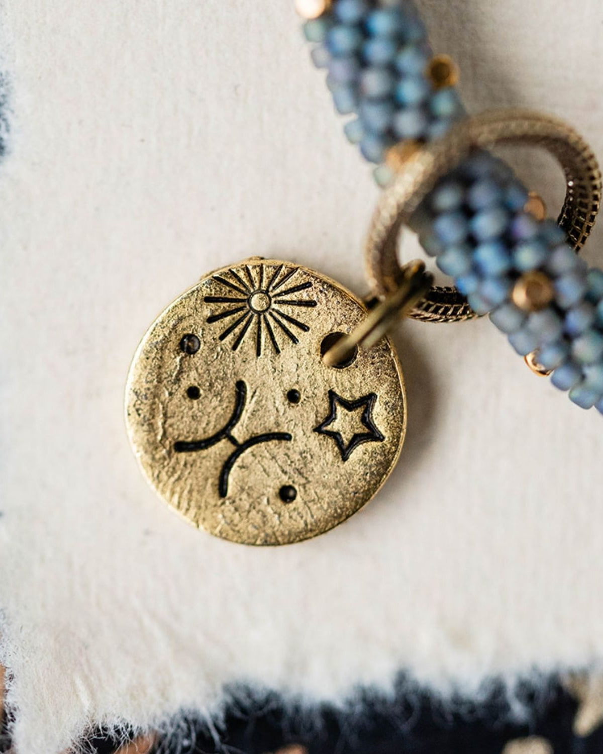 Gold Pisces charm with blue-grey beaded jewelry showing fish constellation and sun engravings
