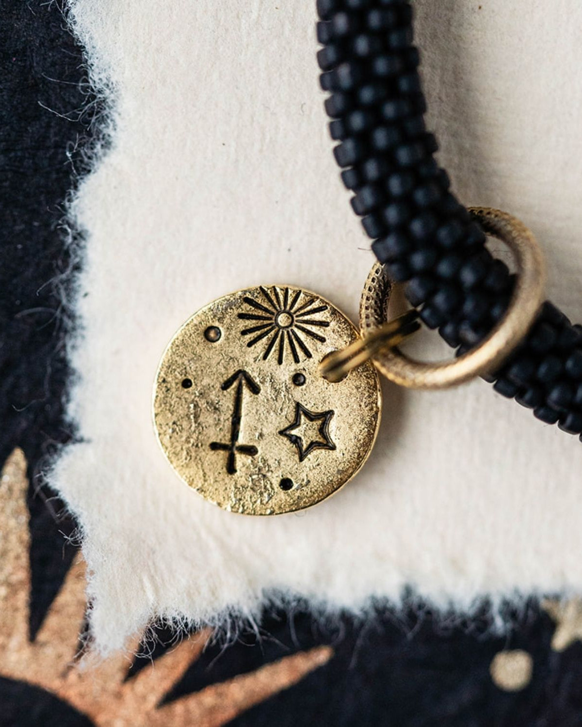 Close-up gold Sagittarius zodiac charm with archer bow attached to black beaded jewelry