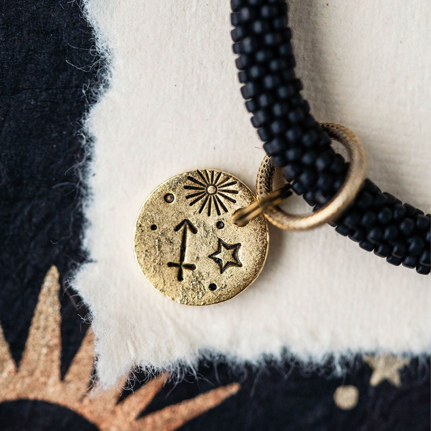 Close-up gold Sagittarius zodiac charm with archer bow attached to black beaded jewelry