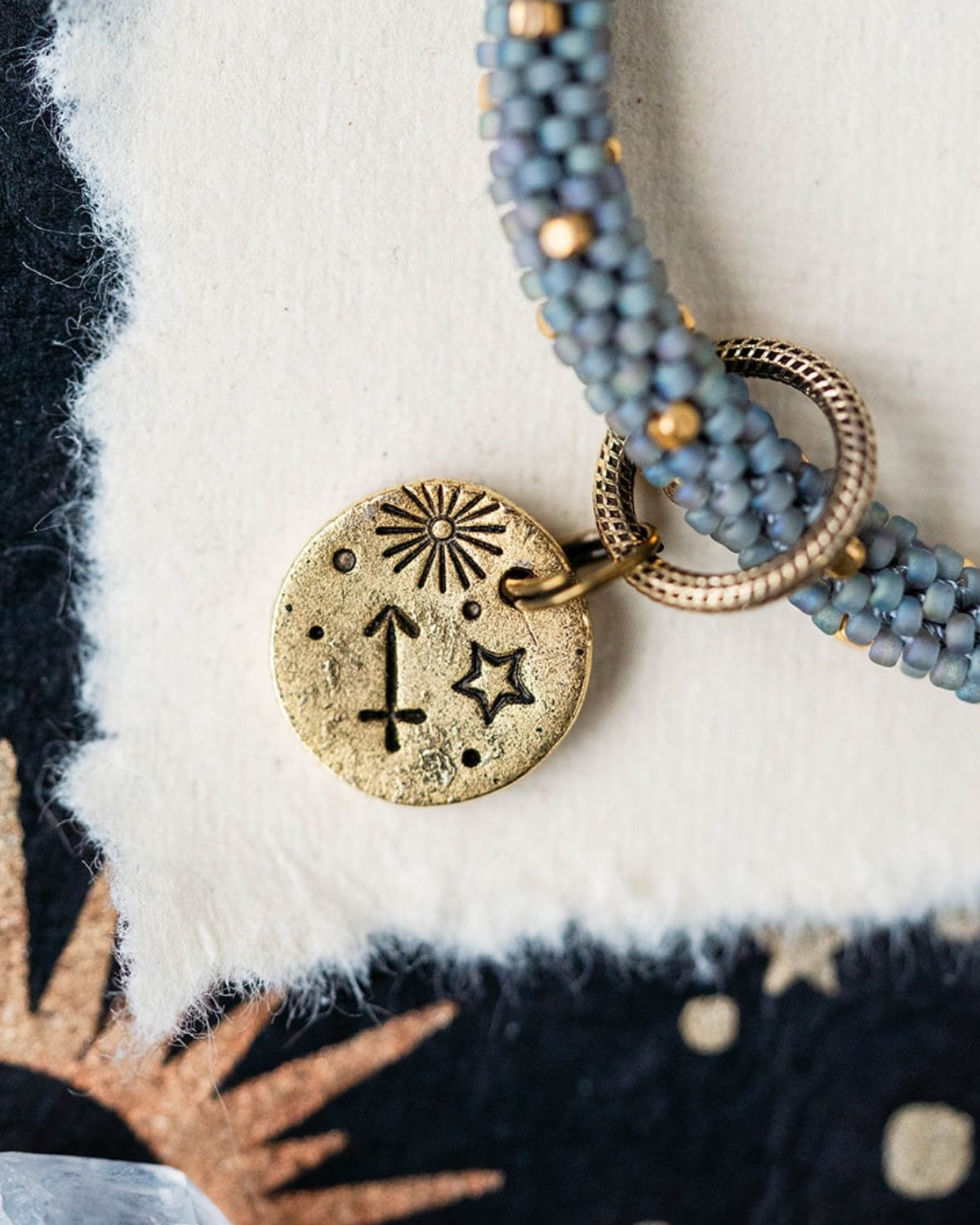 Gold Sagittarius charm with blue-grey beaded strands showing archer constellation and sun engravings
