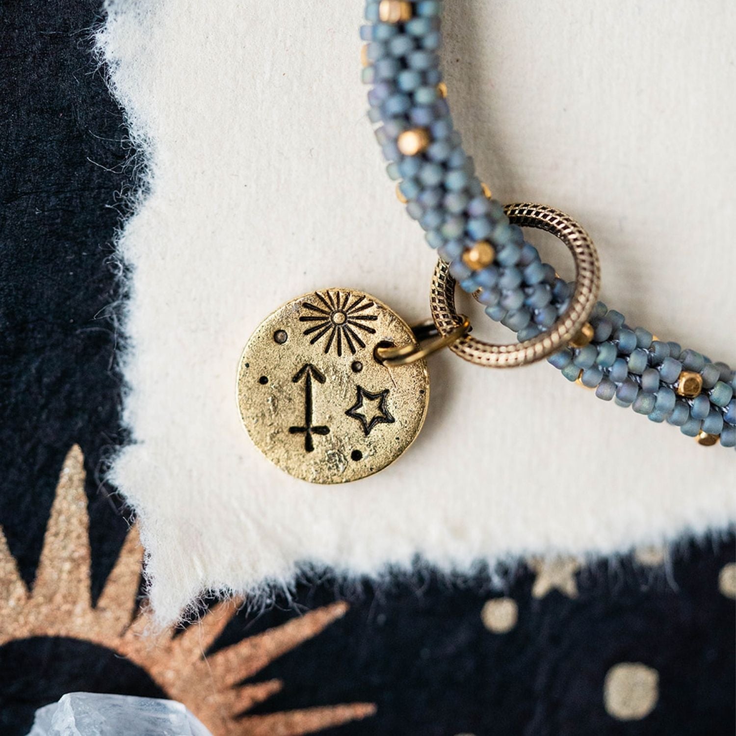 Gold Sagittarius charm with blue-grey beaded strands showing archer constellation and sun engravings