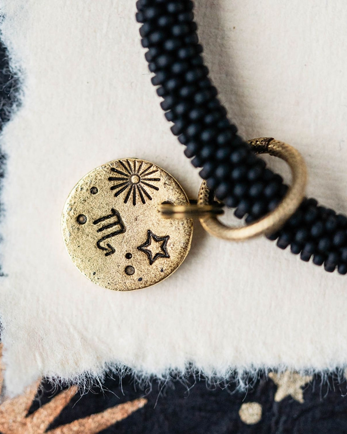 Close-up gold Scorpio zodiac charm with constellation symbols attached to black beaded bracelet