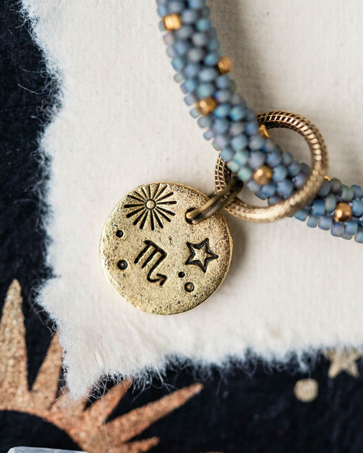 Gold Scorpio zodiac pendant with blue-grey beaded jewelry showing scorpion constellation engravings