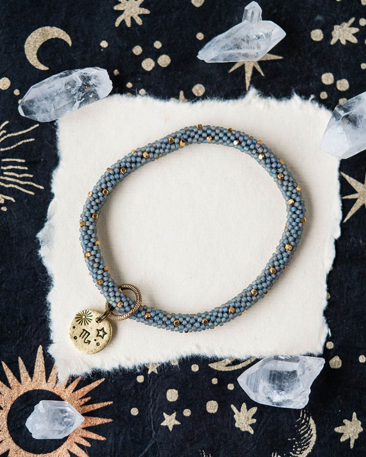 Blue-grey beaded bracelet with gold spacers and Scorpio zodiac charm styled with clear crystals