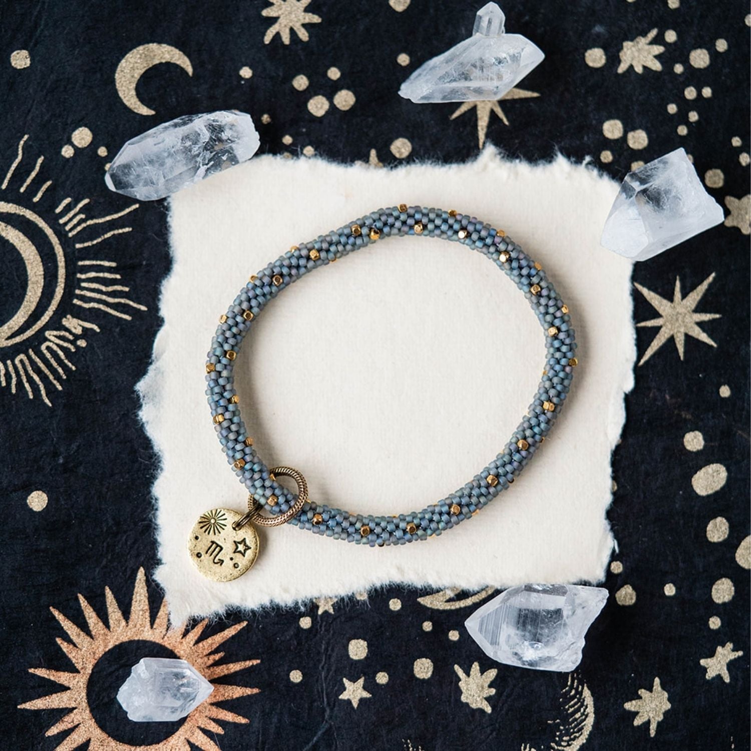 Blue-grey beaded bracelet with gold spacers and Scorpio zodiac charm styled with clear crystals