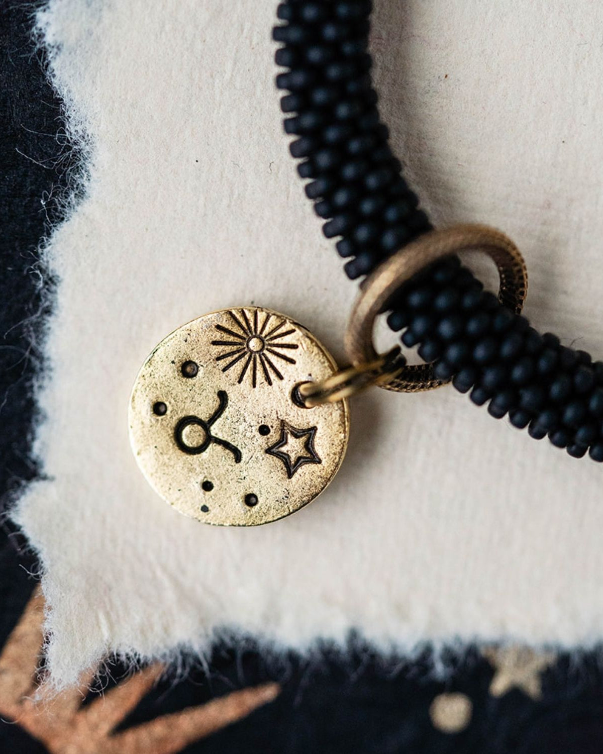 Close-up gold Taurus zodiac charm with bull symbols attached to black beaded bracelet detail
