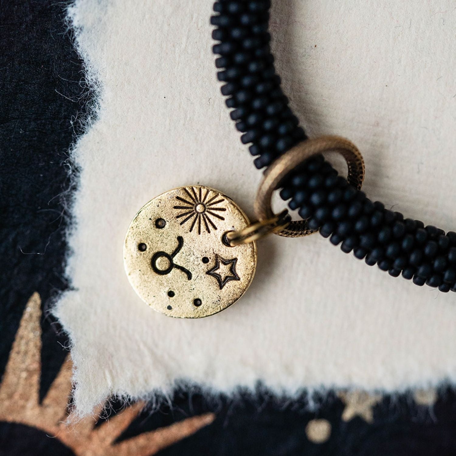 Close-up gold Taurus zodiac charm with bull symbols attached to black beaded bracelet detail
