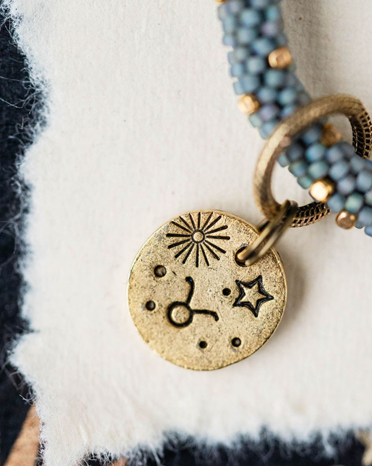 Gold Taurus charm with blue-grey beaded jewelry showing bull constellation and sun engravings