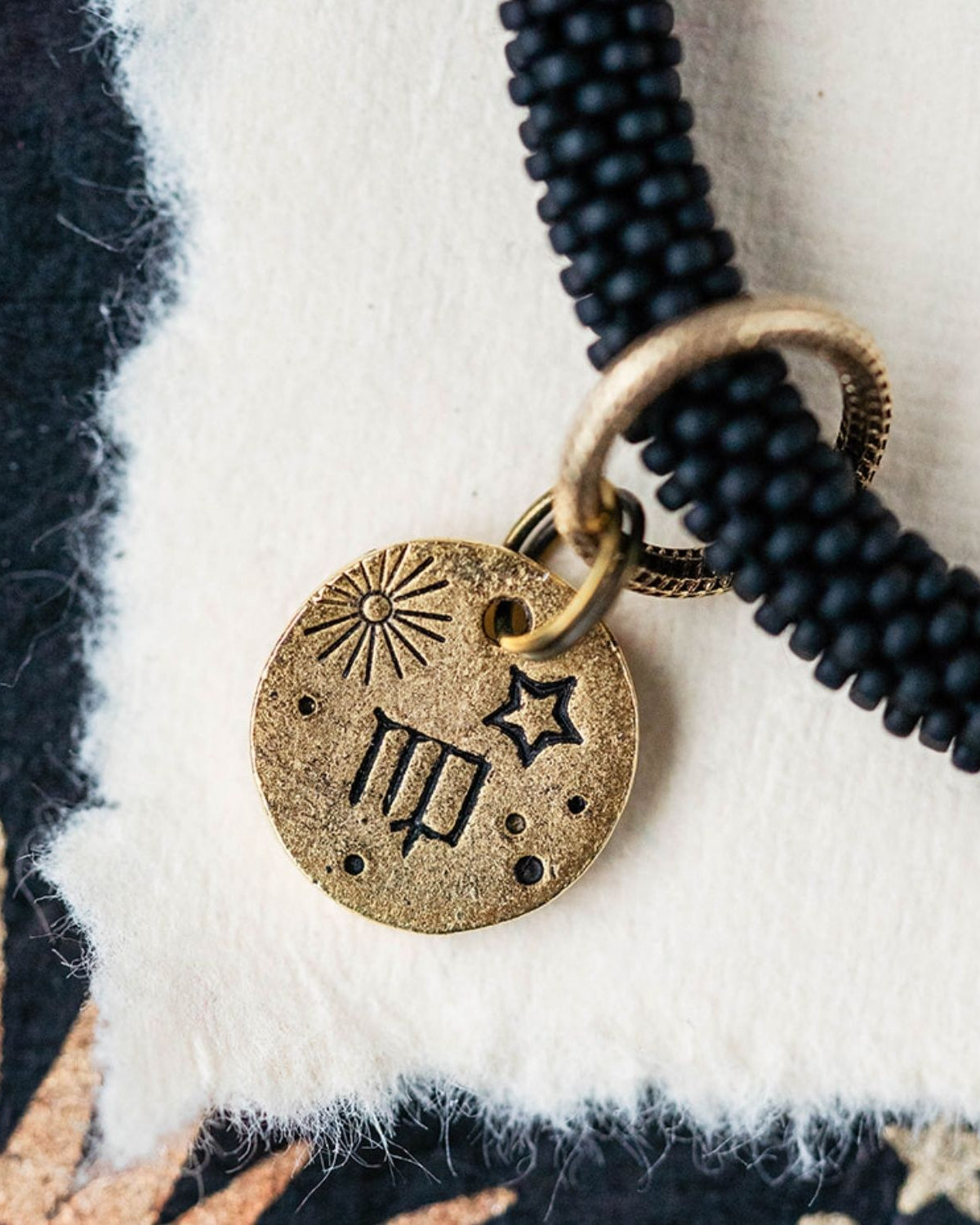Close-up gold Virgo zodiac charm with maiden symbols attached to black beaded bracelet detail