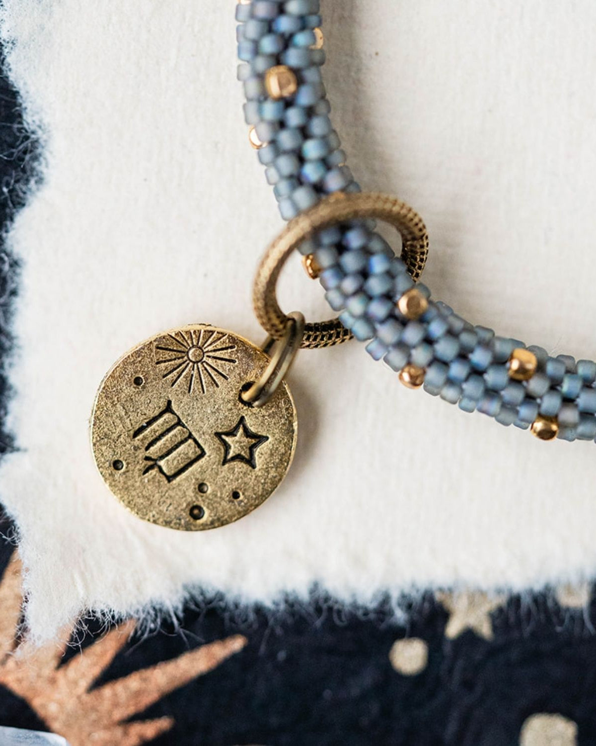 Gold Virgo charm with blue-grey beaded jewelry showing constellation and wheat engravings