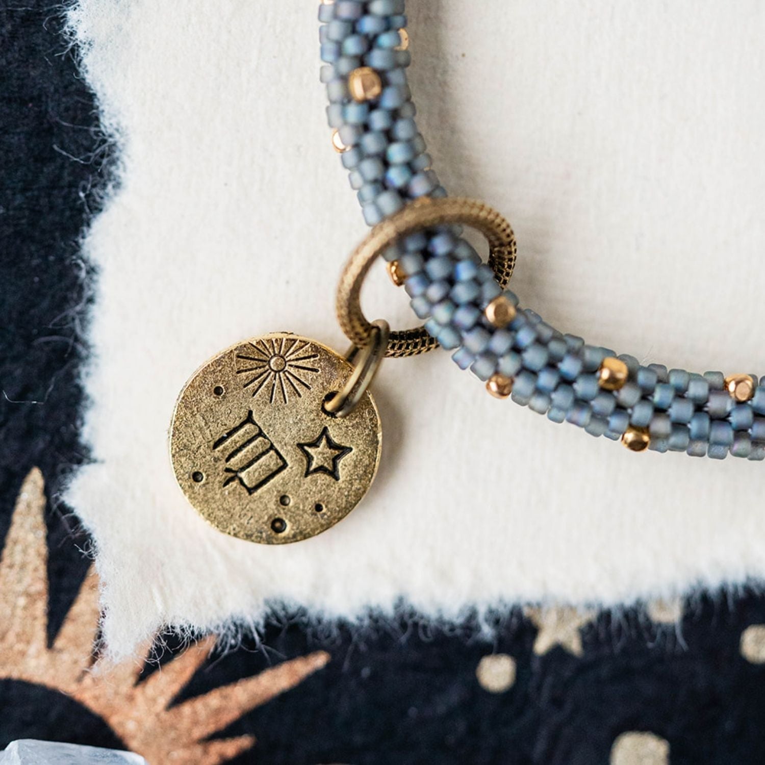 Gold Virgo charm with blue-grey beaded jewelry showing constellation and wheat engravings