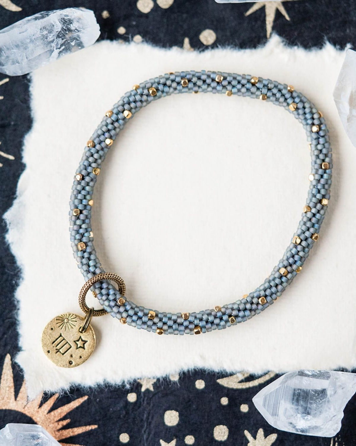 Blue-grey beaded bracelet with gold spacers and Virgo zodiac charm on starry background
