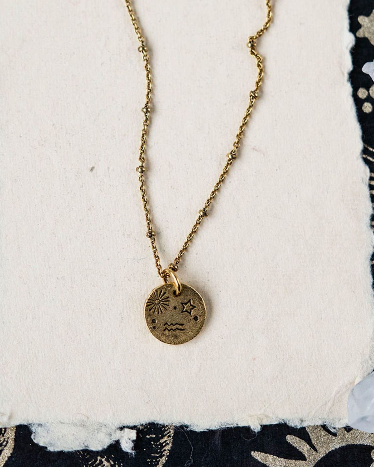 Aquarius constellation charm necklace featuring gold disc pendant with sun star and wave engravings