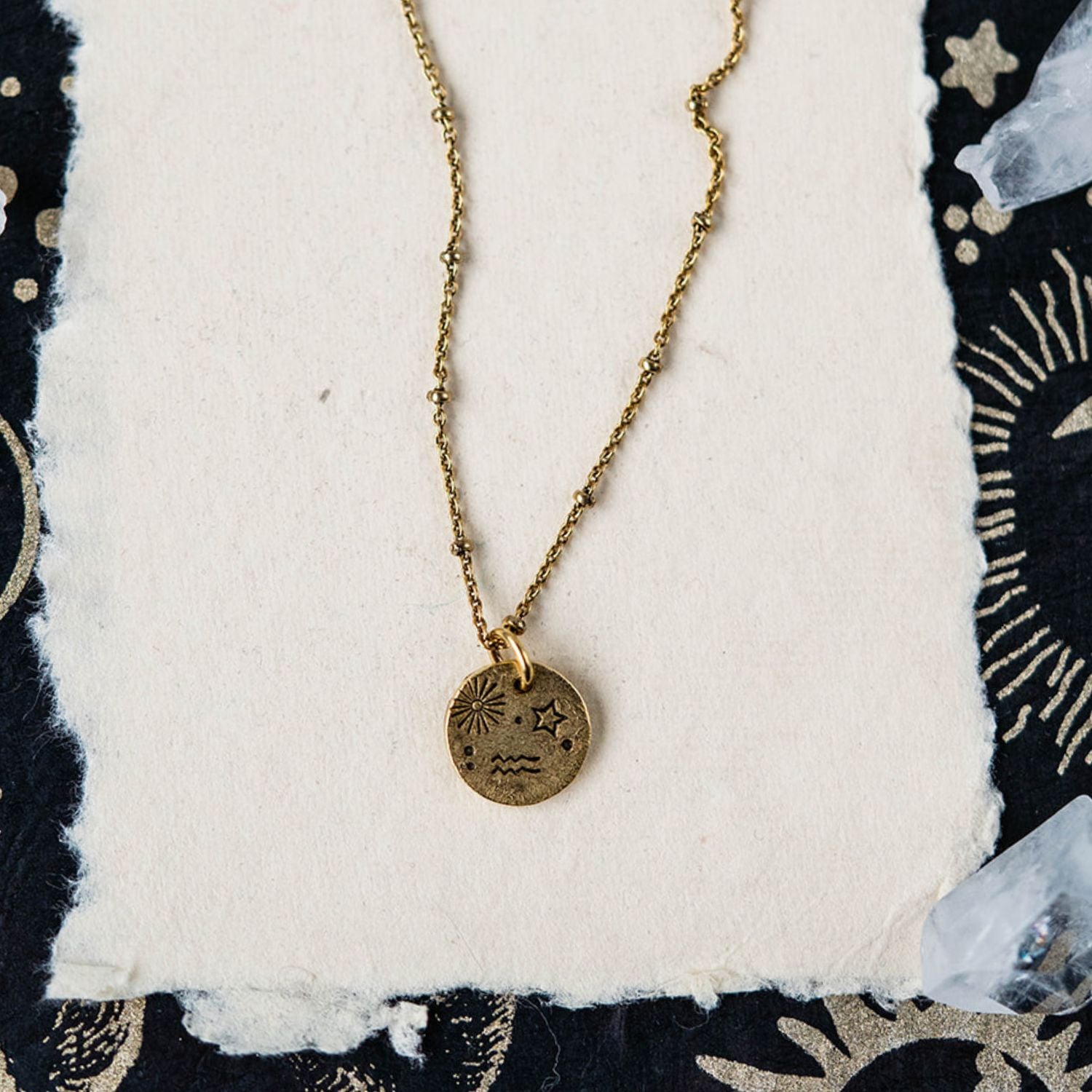 Aquarius constellation charm necklace featuring gold disc pendant with sun star and wave engravings