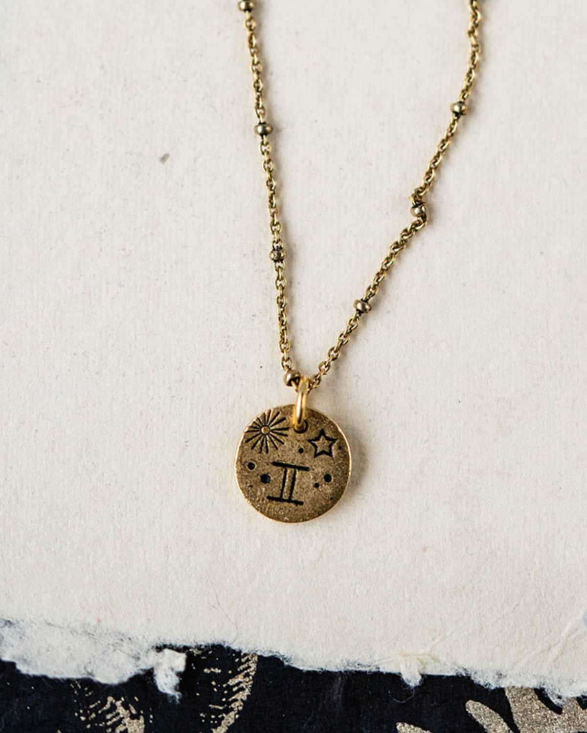 Gemini constellation charm necklace featuring gold disc with engraved twins and star motifs