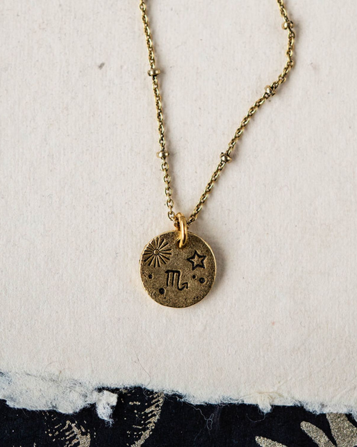 Handcrafted Scorpio zodiac necklace with golden pendant and beaded chain styled on white fabric