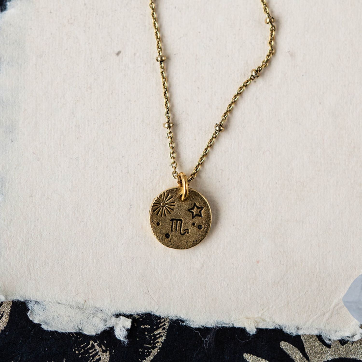 Handcrafted Scorpio zodiac necklace with golden pendant and beaded chain styled on white fabric