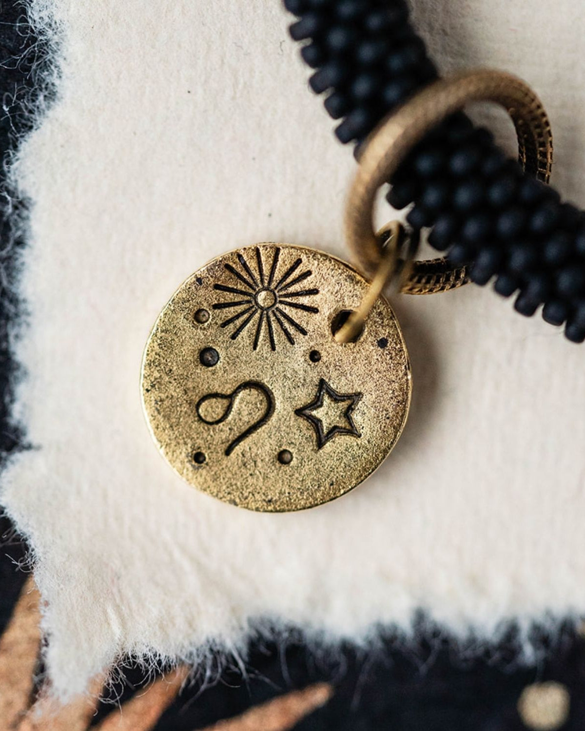 Close-up gold Leo zodiac charm with lion symbol attached to black beaded bracelet detail