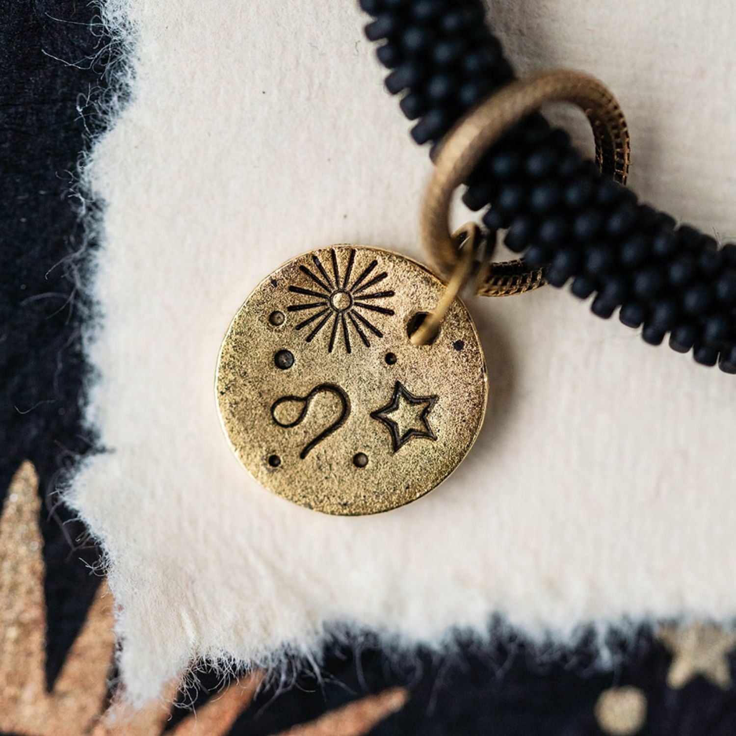 Close-up gold Leo zodiac charm with lion symbol attached to black beaded bracelet detail