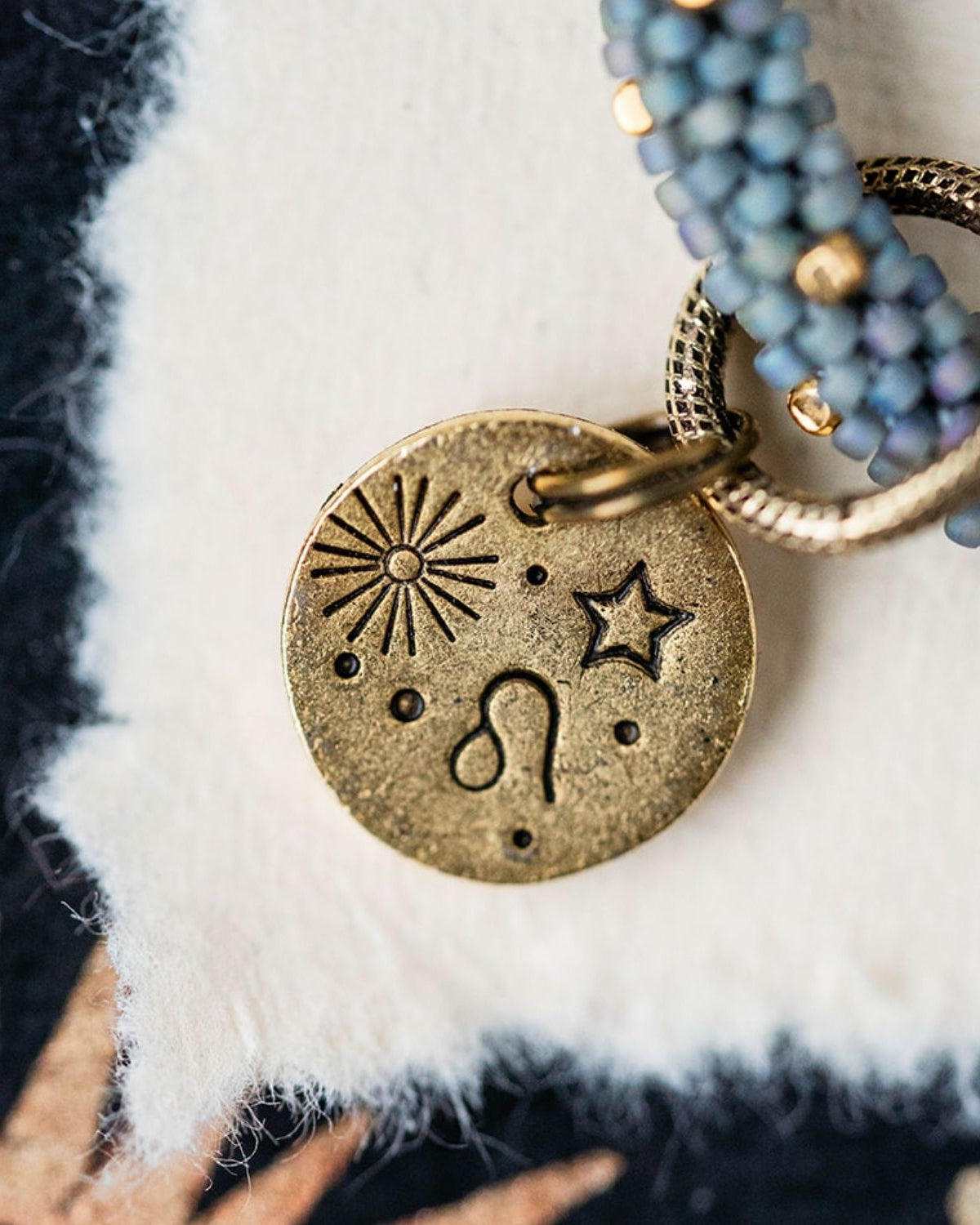 Gold Leo charm with blue-grey beaded jewelry showing lion constellation and sun engravings