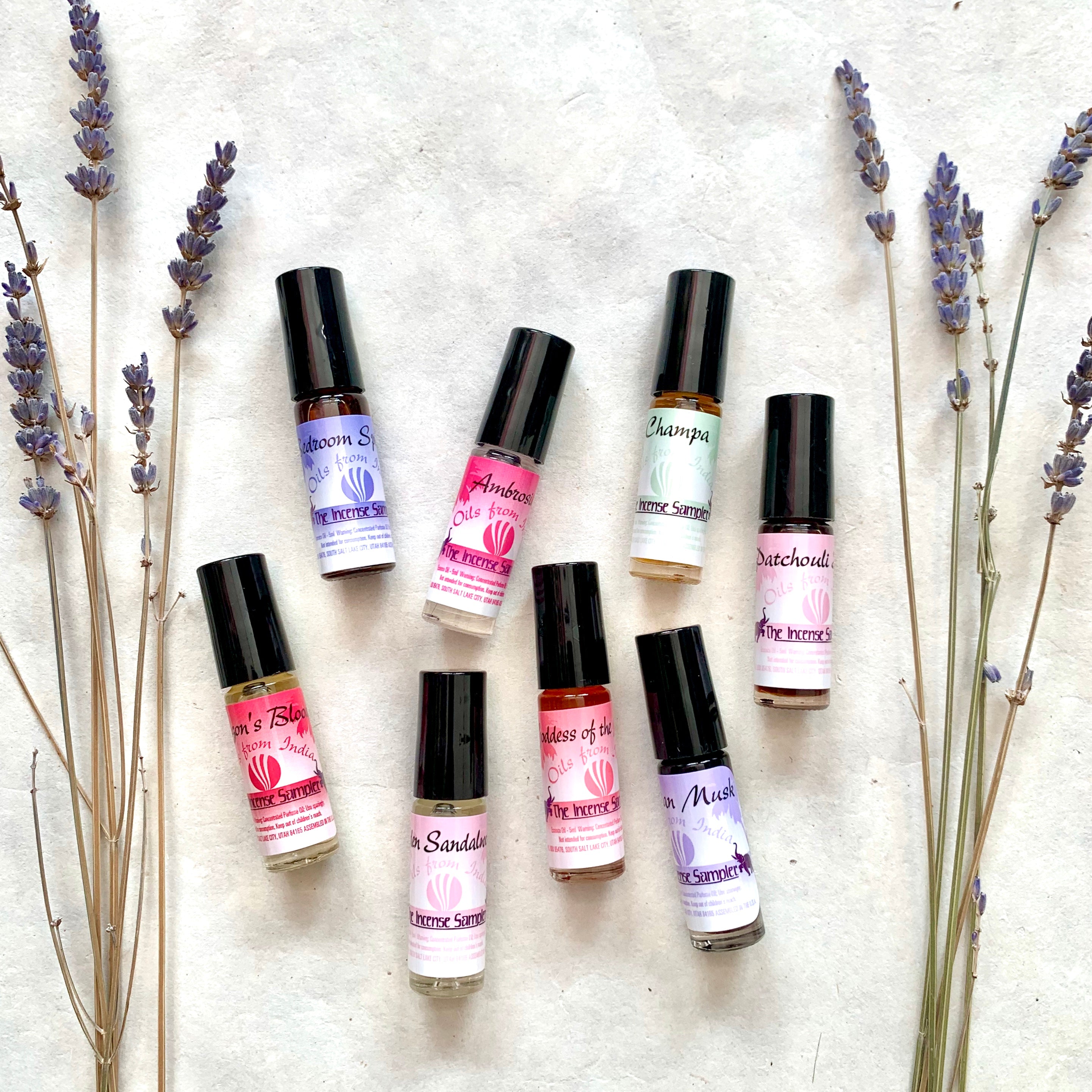 The Incense Sampler perfume oil collection from India displayed with dried lavender, featuring eight scents including Ambrosia, Bedroom Special, Champa, and Egyptian Musk in roll-on glass vials.