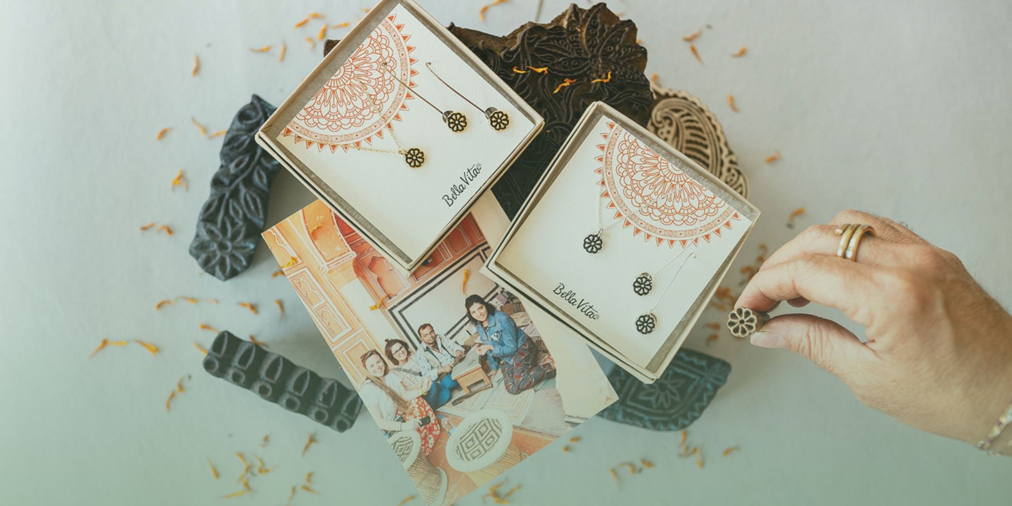 Bella Vita Jewelry set with floral design in elegant packaging, hand picking a piece. Below, a photo of smiling community members.