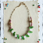 Necklace with green and white beads on a textured card against a black and white patterned background.