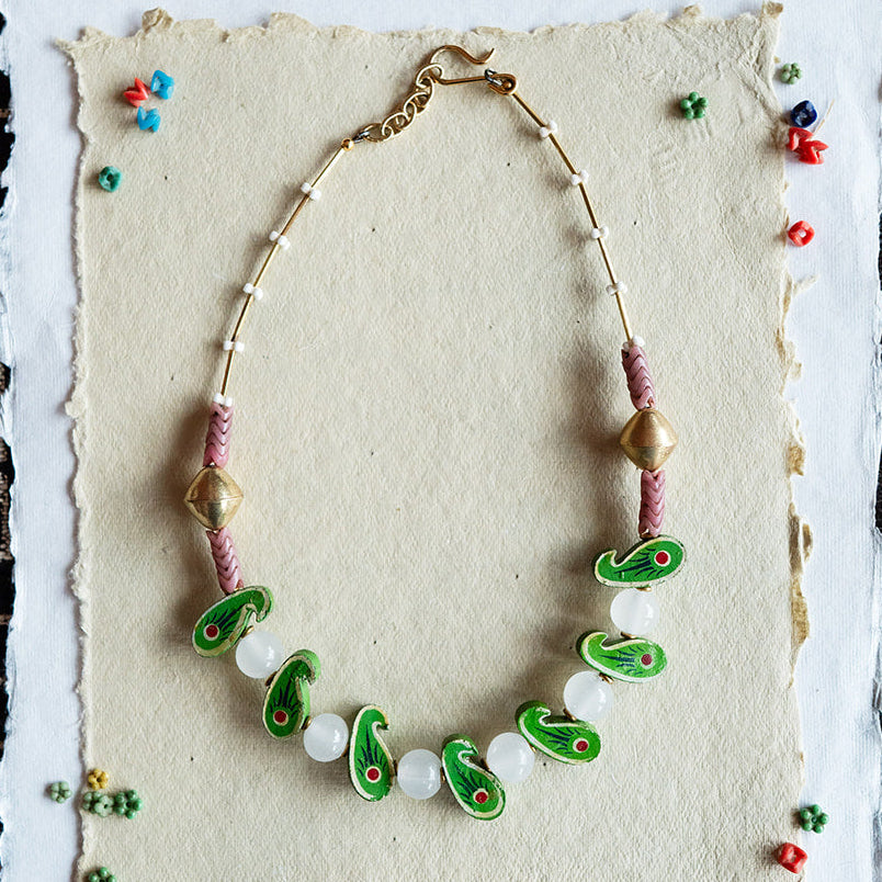 Necklace with green and white beads on a textured card against a black and white patterned background.