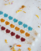 Three handmade beaded friendship bracelets with repeating heart patterns in teal, orange, and burgundy on a white background, styled with dried flower petals.