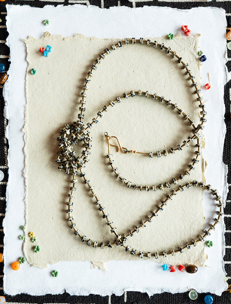 Three beaded necklaces on a textured white card with a black and white geometric patterned background.