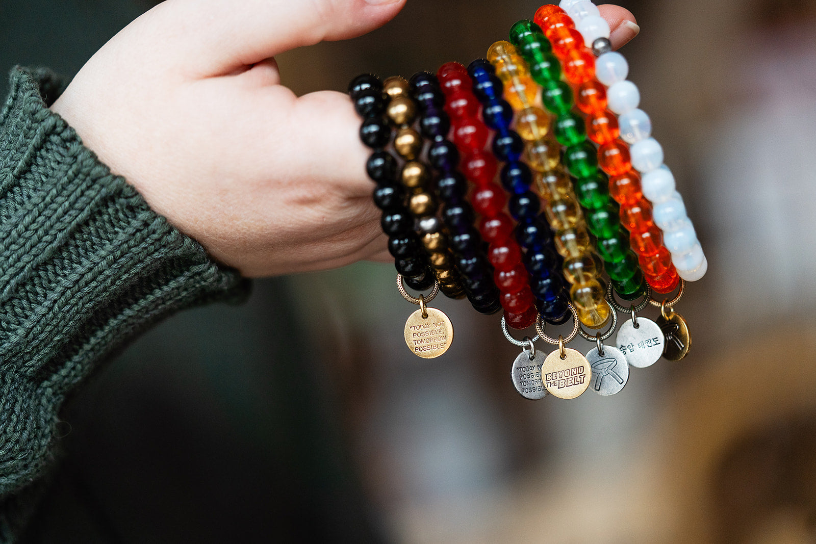 Hand holding a set of colorful beaded bracelets with metal tags.