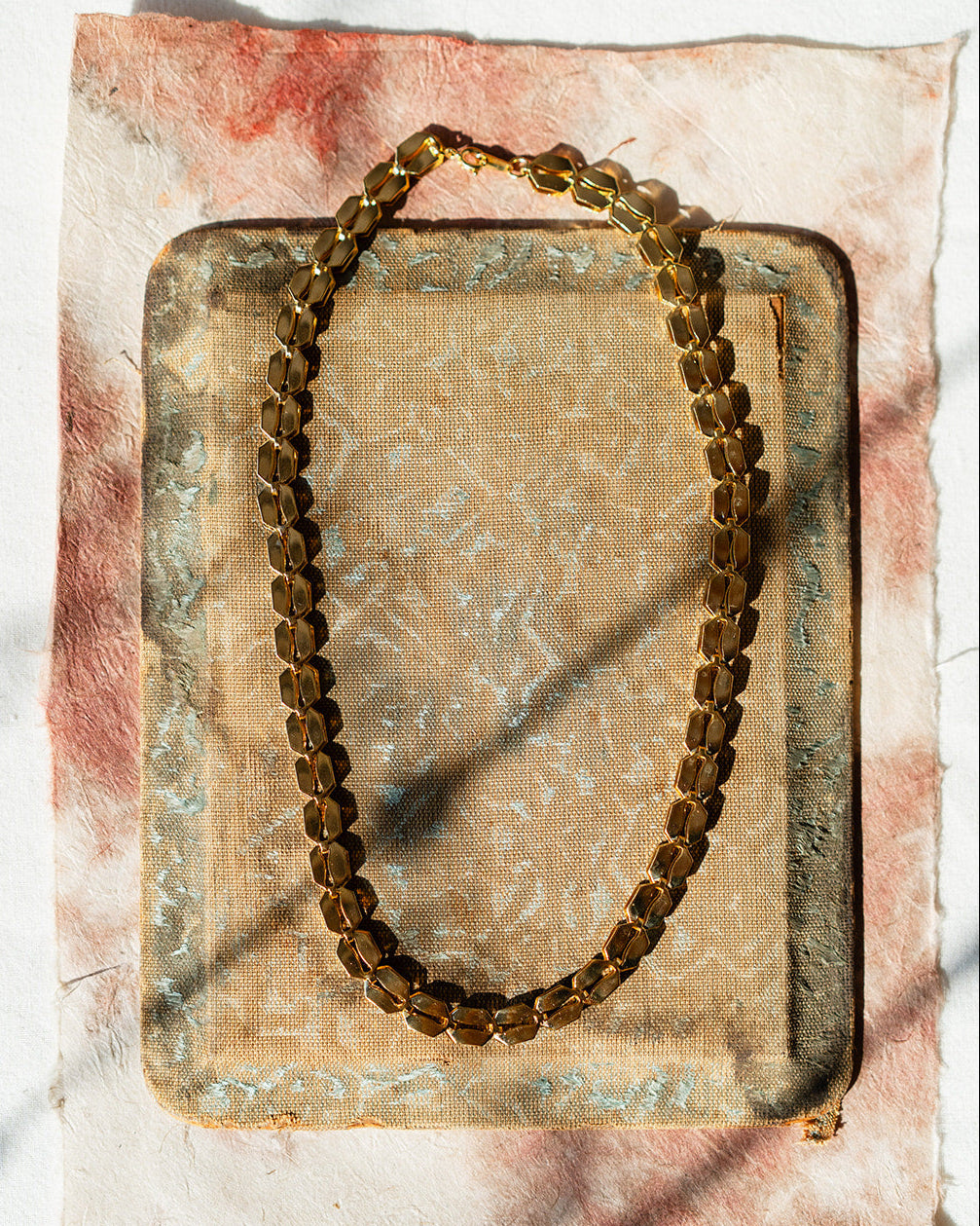Gold chain necklace on a textured surface with a white background
