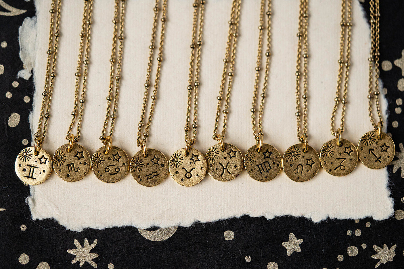 Set of gold necklaces with zodiac symbols on a black background with star designs