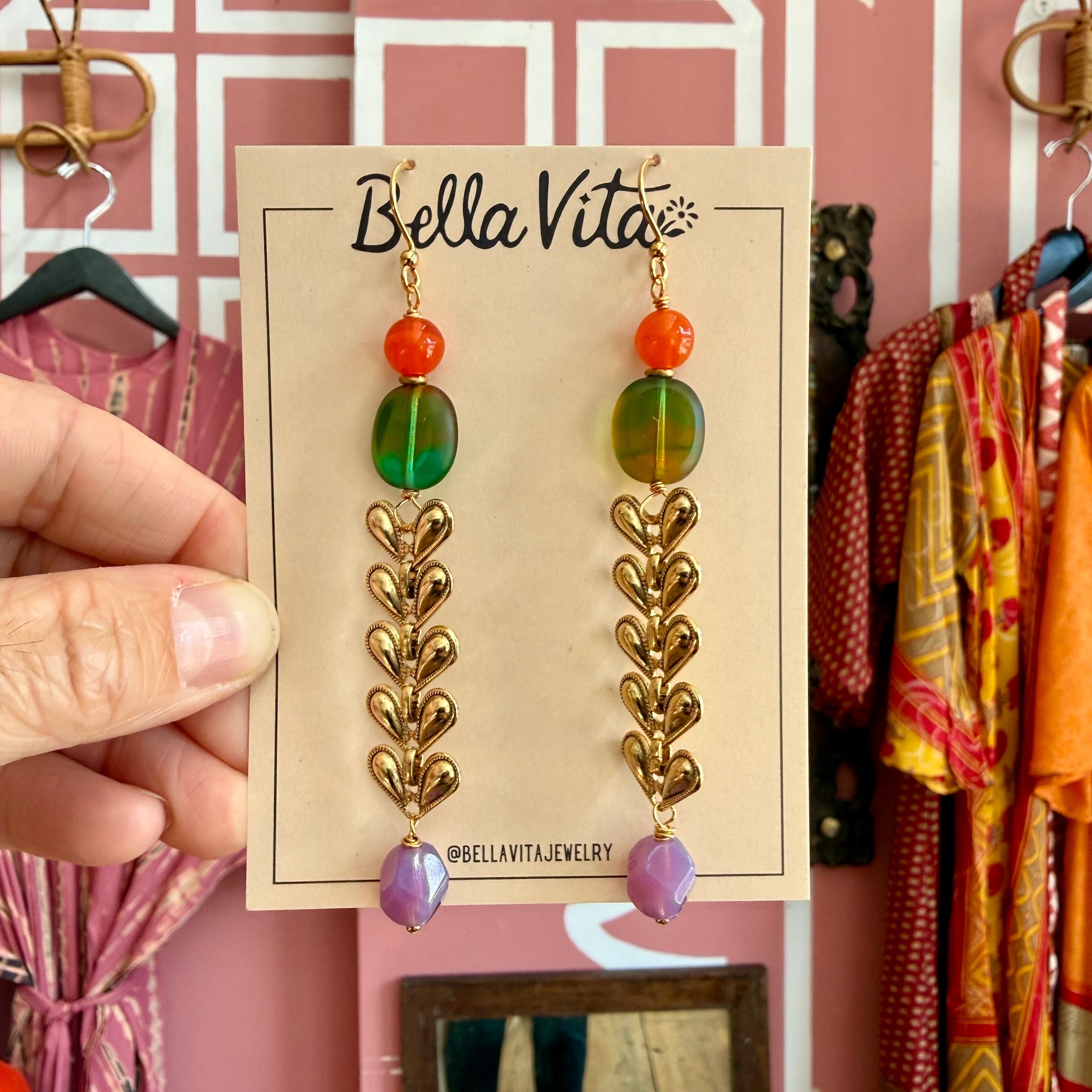 Bella Vita earrings on a card with a pink background and clothing items.