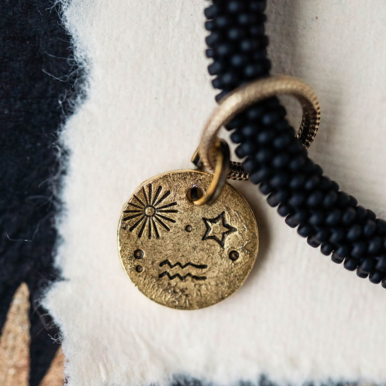 Close-up detail of gold Aquarius zodiac charm showing engraved sun starburst star and water bearer waves