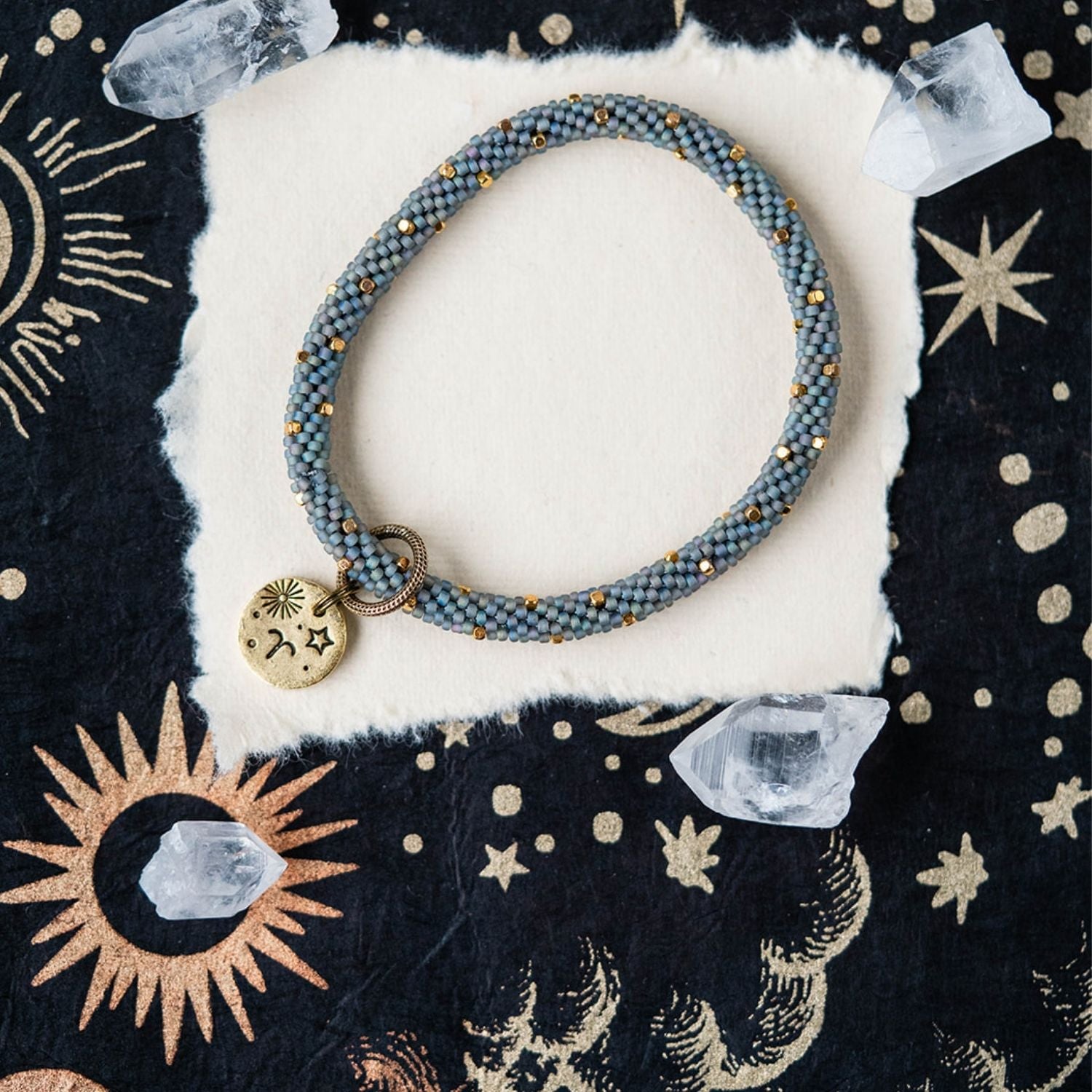 Blue-grey beaded bracelet with gold spacers and Aries zodiac charm on starry background