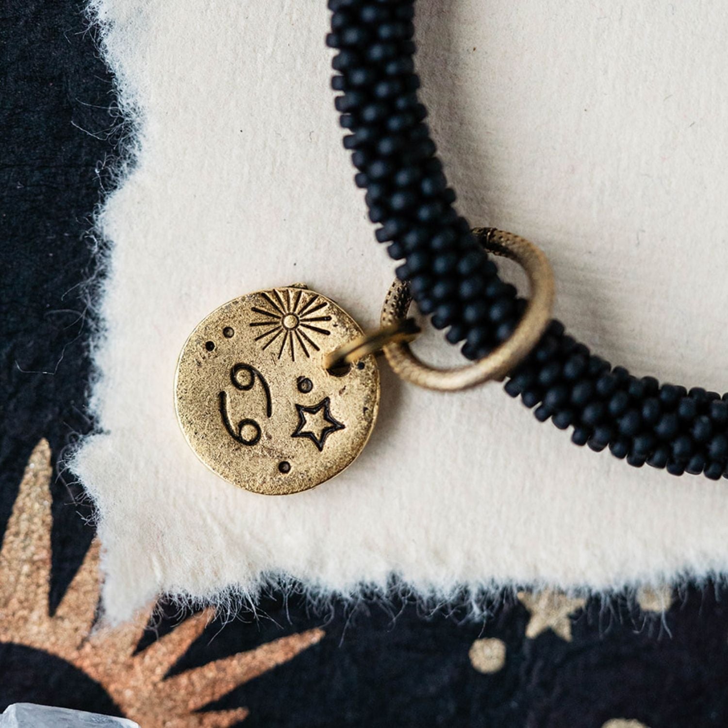Close-up Cancer zodiac charm with crab engravings attached to black beaded bracelet detail