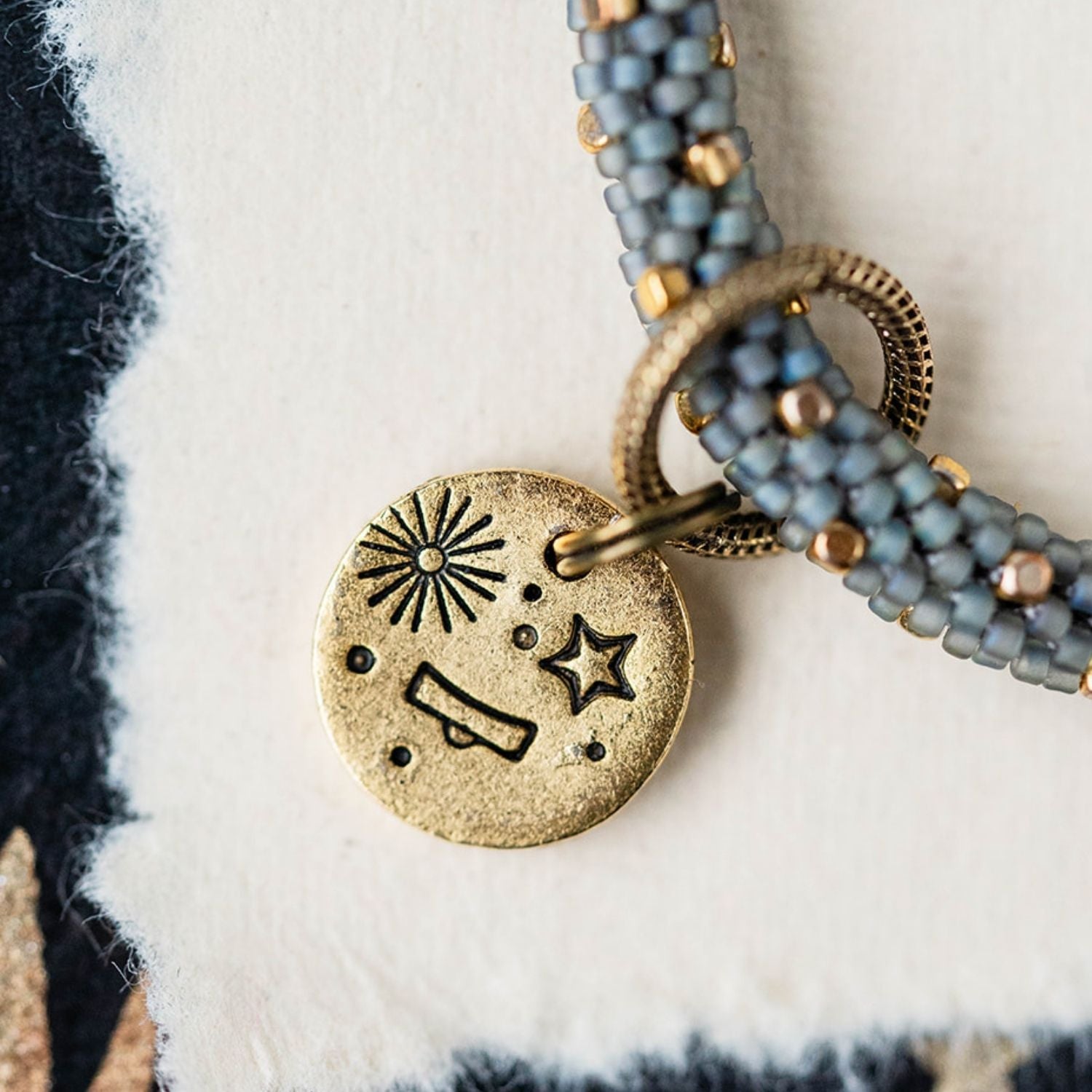 Gold Libra charm with blue-grey beaded strands showing scales constellation and sun engravings