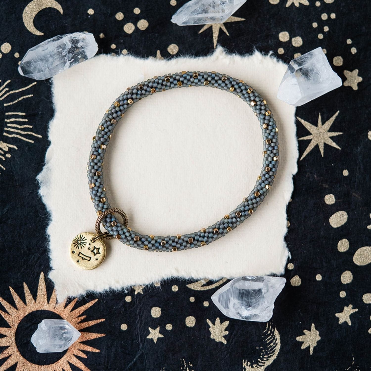 Blue-grey beaded bracelet with gold accents and Libra zodiac charm on celestial background