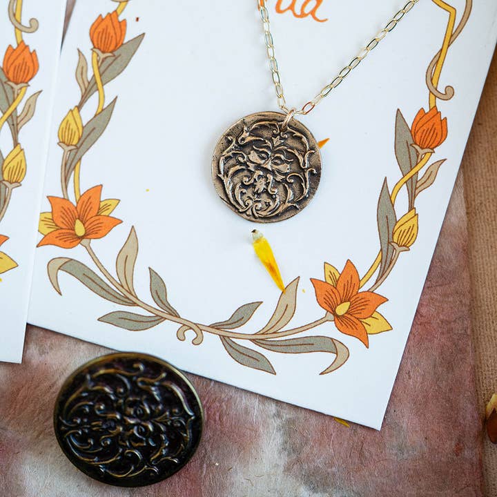 The Art Nouveau Man Necklace displayed on an illustrated card, highlighting its vintage-inspired bronze design.